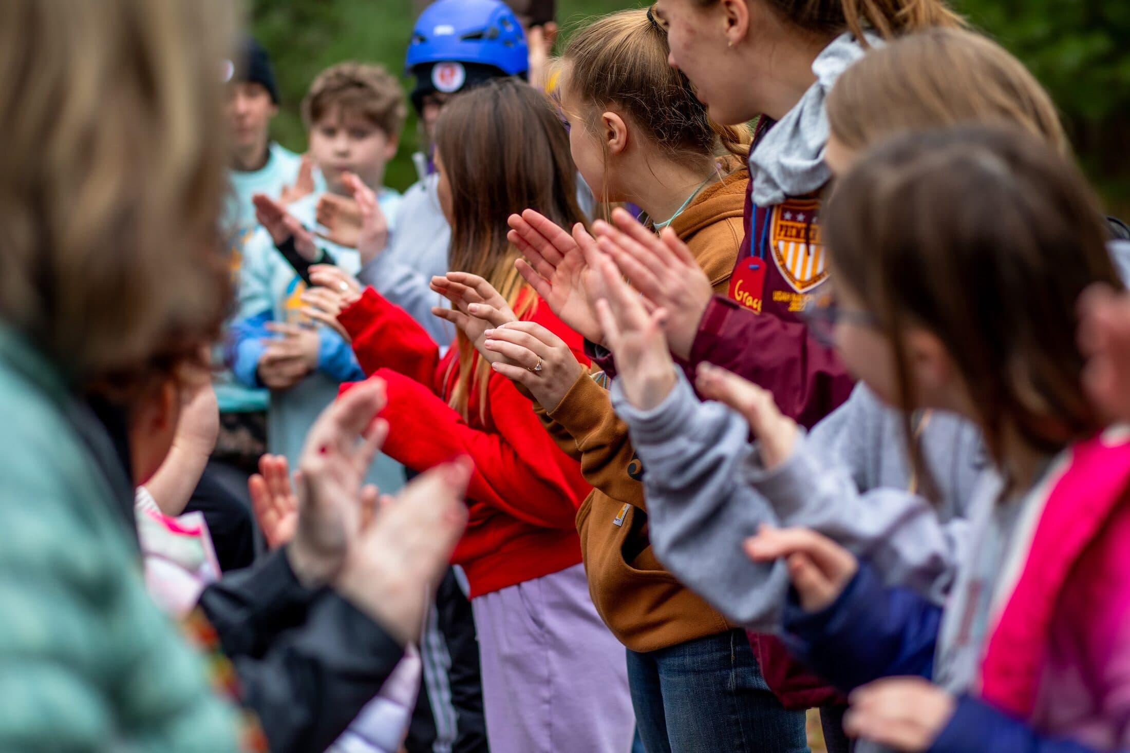 A row of children applauding together, hands raised mid-clap, at a Camp HOPE gathering.