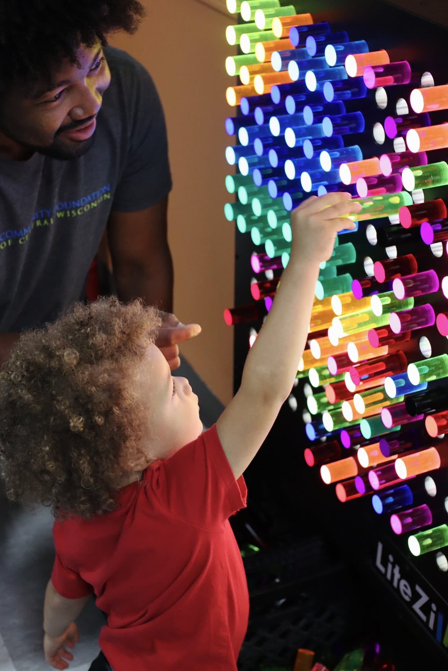 A child and an adult building a glowing pattern on a light-peg wall at a community space in Stevens Point.