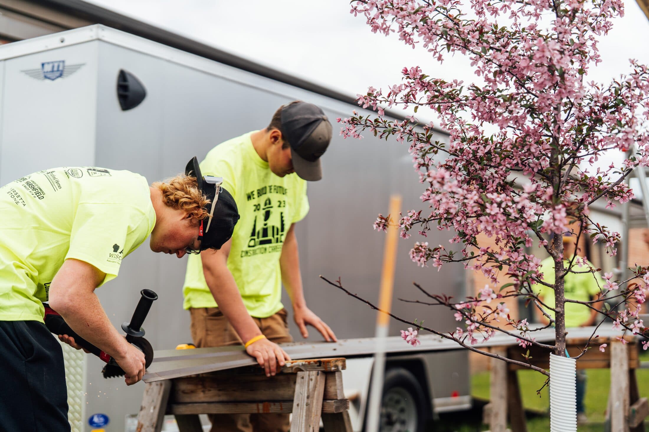 Crew members in high-visibility shirts framing a timber pavilion beside a flowering tree.