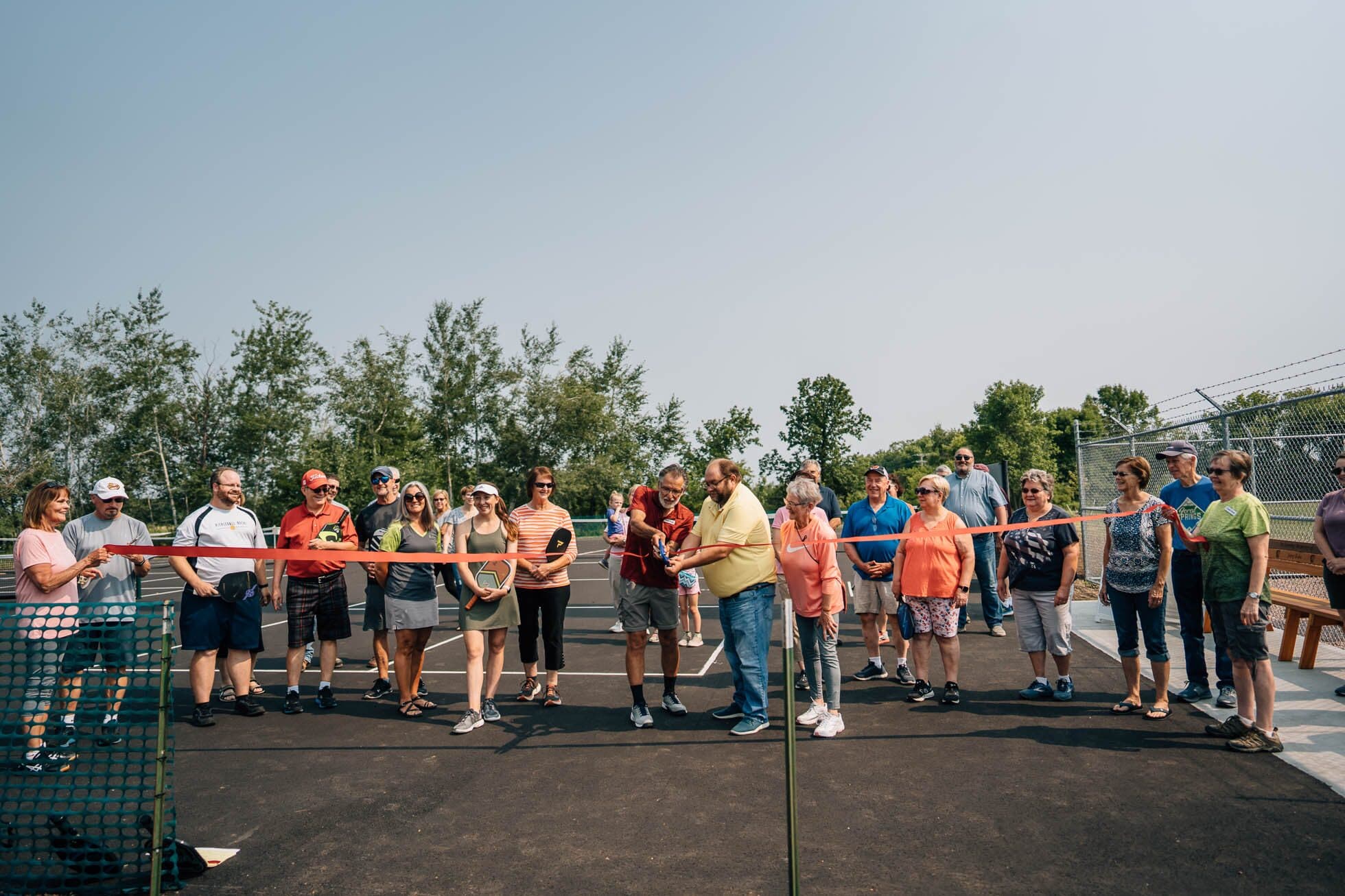 A crowd of neighbors gathered behind a ribbon at the opening of a new community trail.