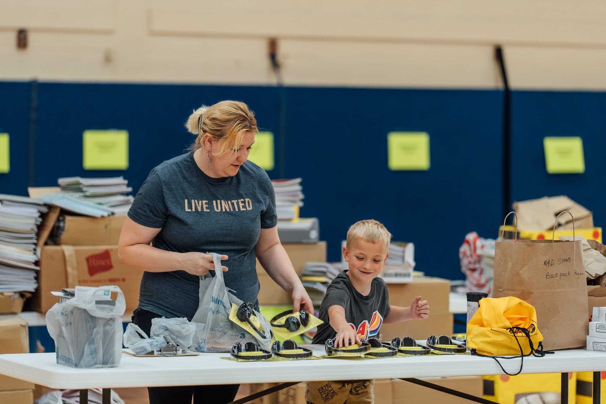 A volunteer and a child sorting donated school supplies across a row of folding tables in Marshfield.